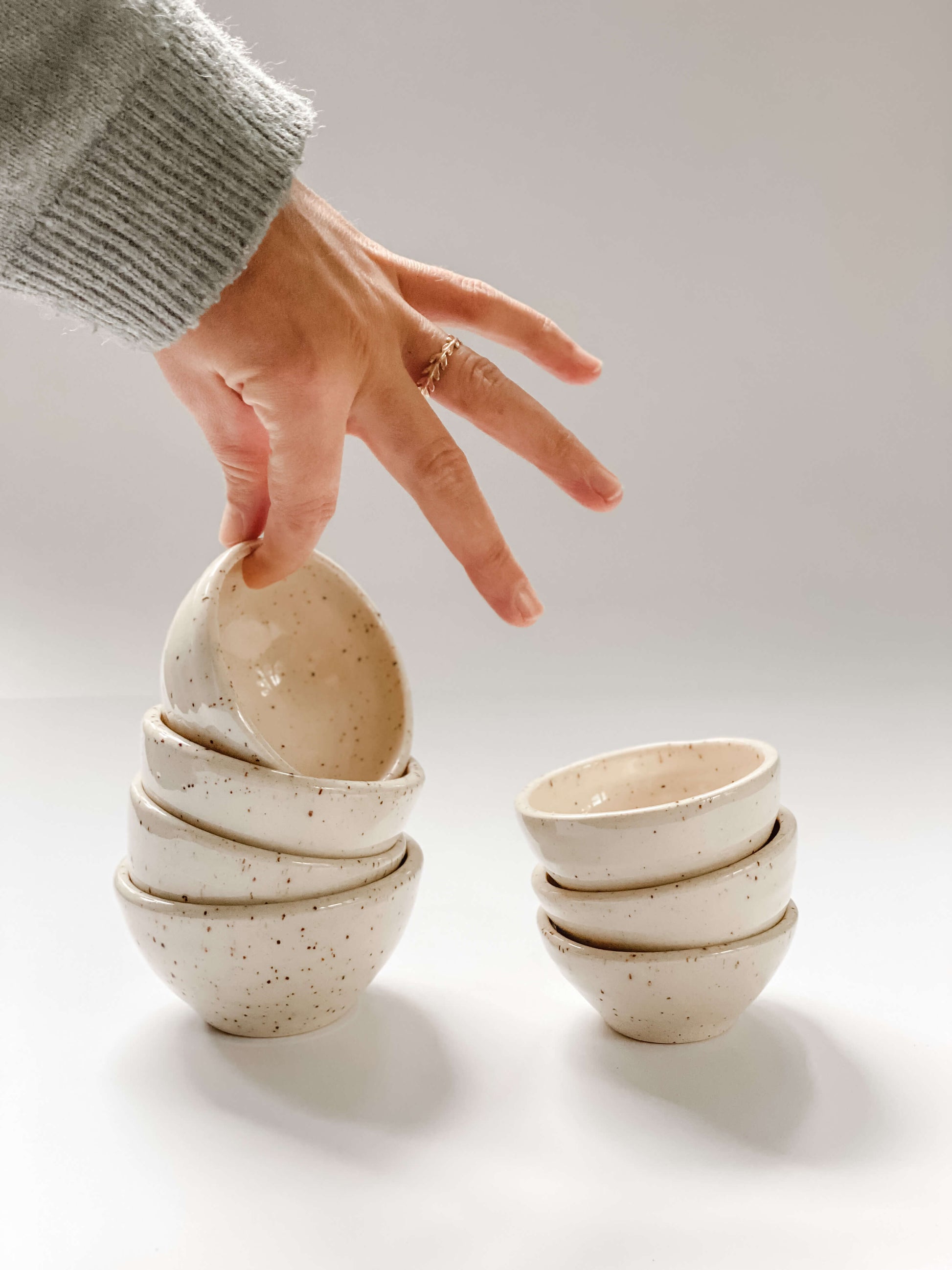 Hand holding up one of 4 stacked small bowls, and stack of 3 small bowls also pictured