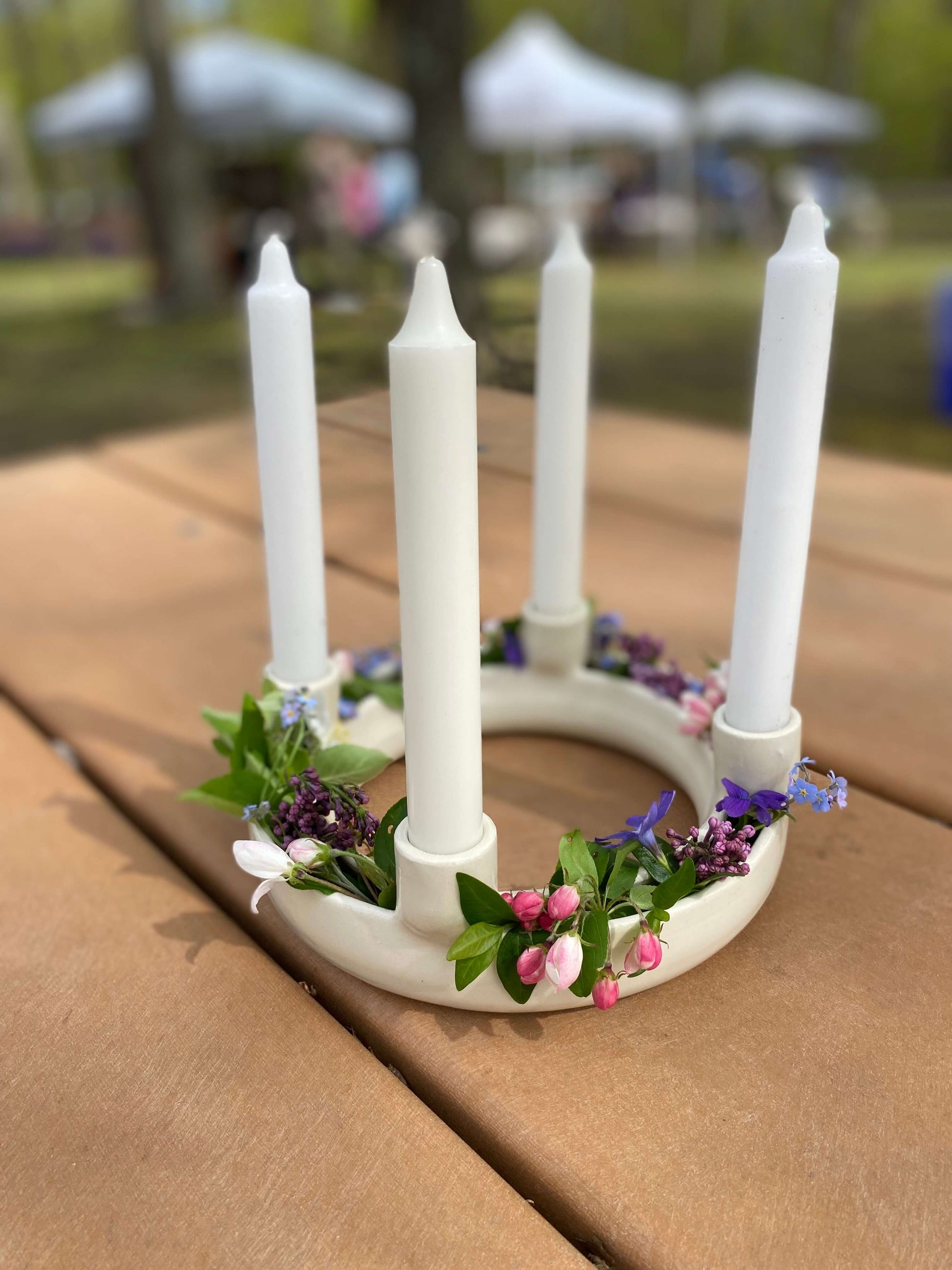 White advent wreath candle holder with four unlit white taper candles, decorated with living spring flowers, lilacs, cherry blossoms, forget me nots, used as a beautiful centerpiece on the table