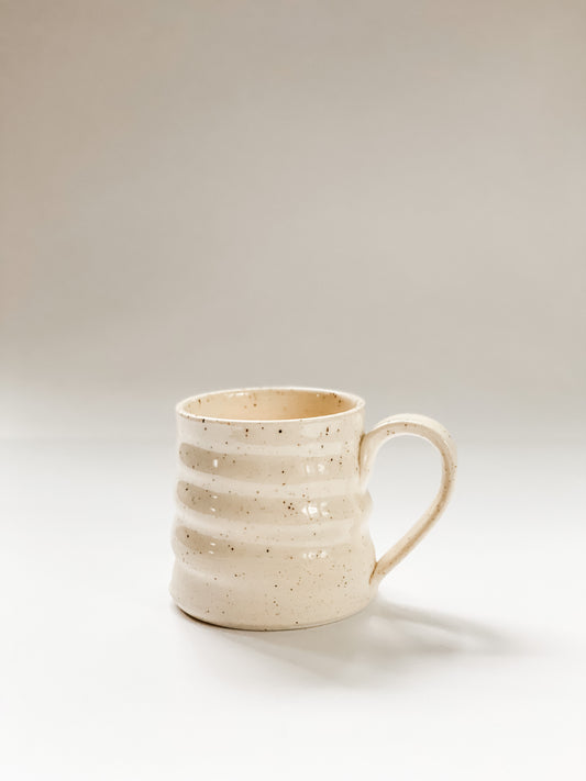 Wheel thrown mug with pronounced spiral throwing marks in cream and brown speckled clay