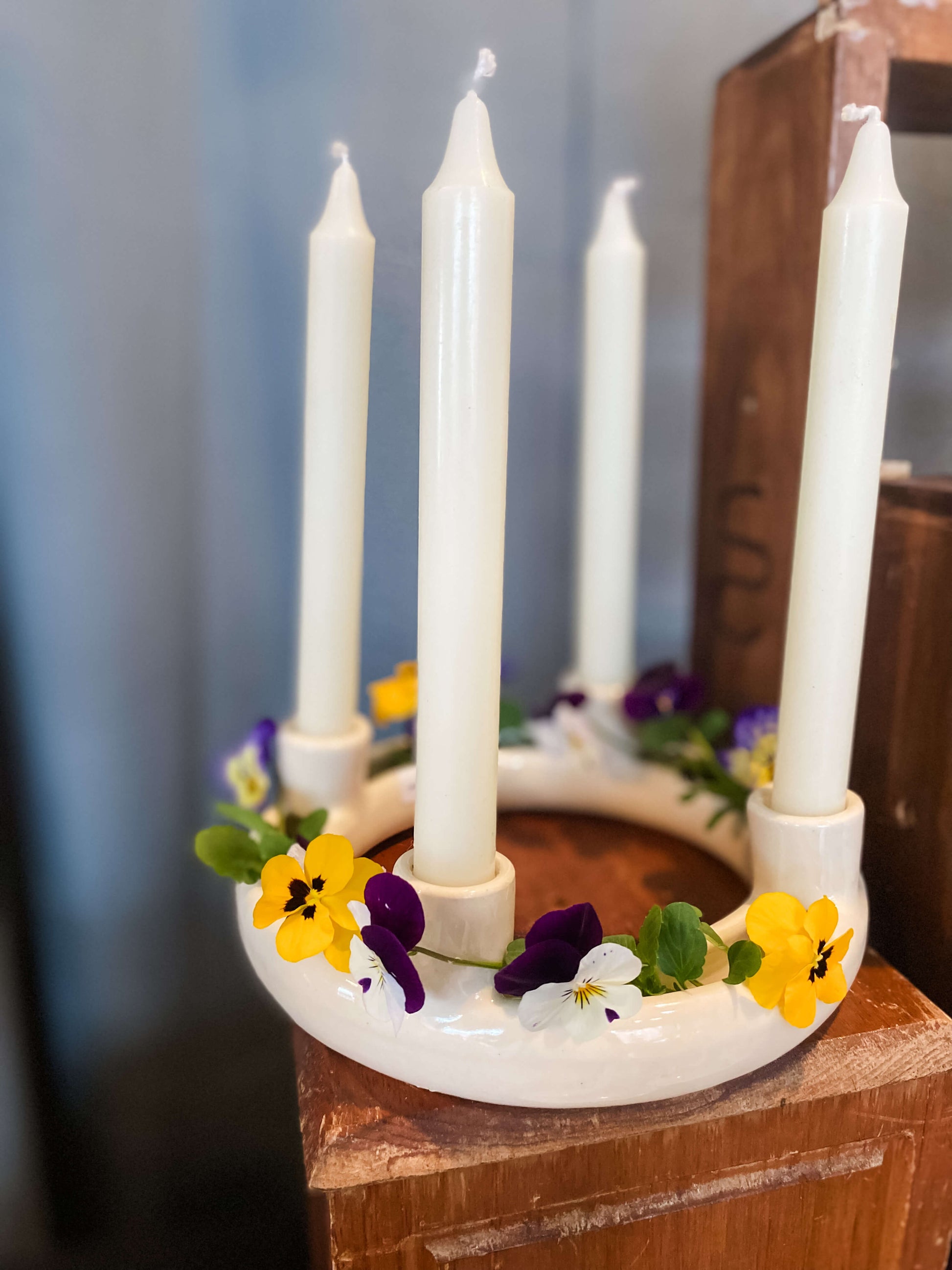White porcelain advent wreath candle holder with 4 unlit tapered candles decorated with living pansies in purple, white and yellow for a beautiful tablescaping display