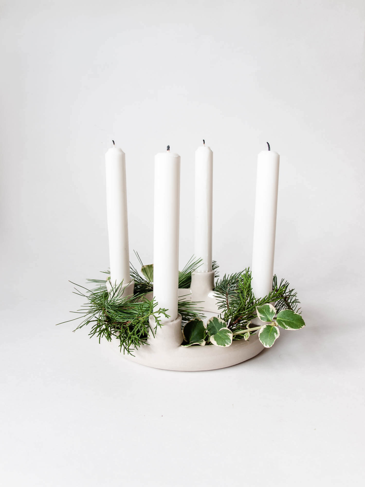 Advent wreath candle holder with four unlit white taper candles, filled with live, green cedar, pine, and holly foliage