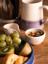 Load image into Gallery viewer, Blue ceramic plate with fruit, small cream and speckled wee bowl with nuts, purple and cream handmade mug in the background
