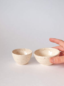 Small wheel thrown ramekins (2) in cream with brown speckled clay. One slightly smaller, one slightly larger with fingers holding it 