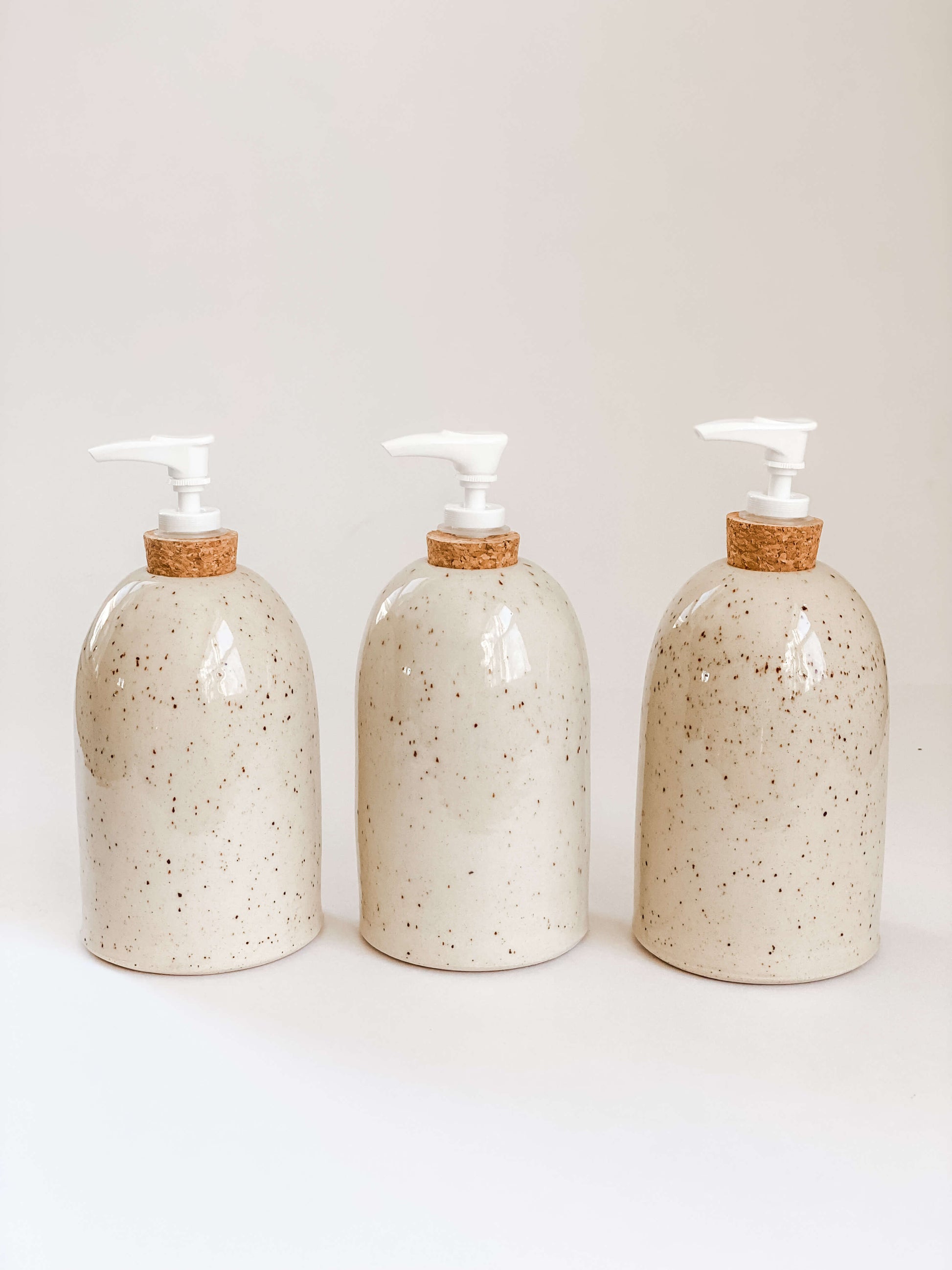 3 speckled stoneware pottery soap pumps lined up to show each is slightly different and one of a kind