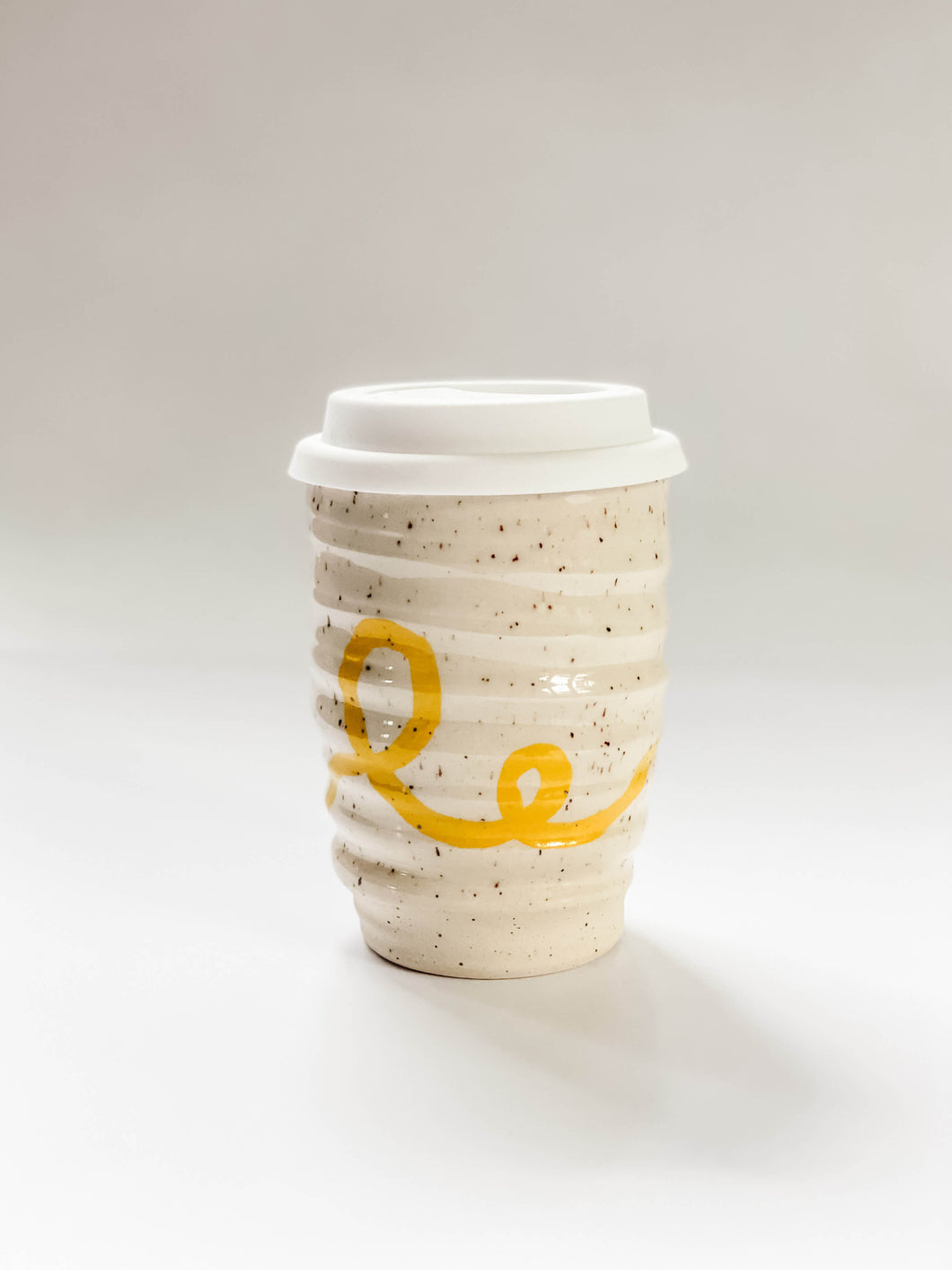 Wheel thrown travel mugs in cream and brown speckled clay with hand painted yellow curving line design 