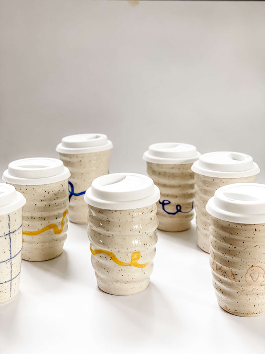 Collection of wheel thrown travel mugs in cream and brown speckled clay with hand painted curving line design