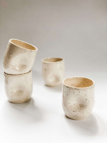 Four wheel thrown tumbler in cream clay with speckles with two dimples pinched into the sides