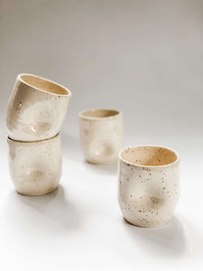 Four wheel thrown tumbler in cream clay with speckles with two dimples pinched into the sides