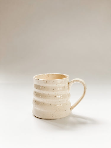 Wheel thrown mug with pronounced spiral throwing marks in cream and brown speckled clay  