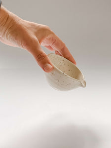 Hand holding a small wheel thrown bowl with a pouring spout in cream clay with speckles