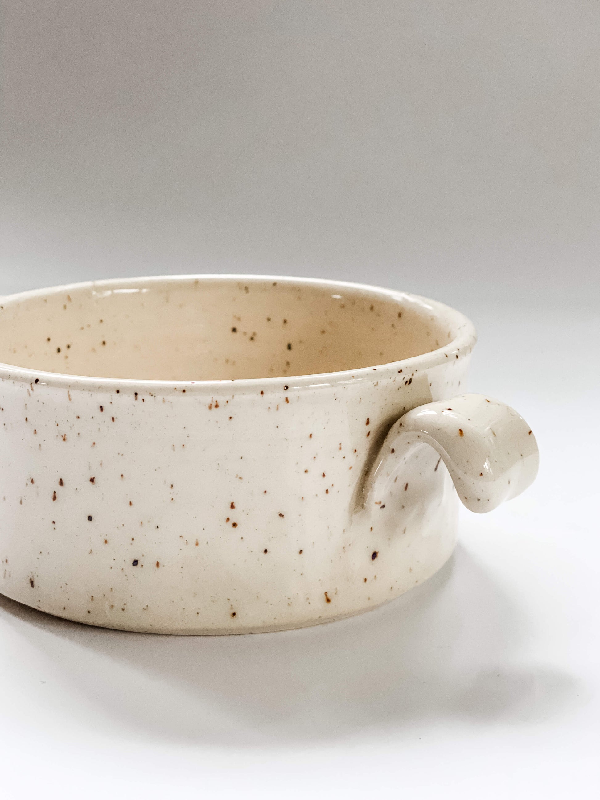 Close up of handle on wheel thrown cylindrical soup bowls with two hooked handles in a cream and brown speckled clay