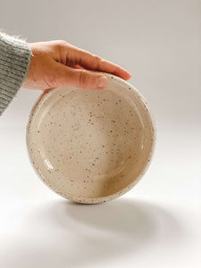 Hand holding a low profile bowls wheel thrown in a cream and brown speckled clay