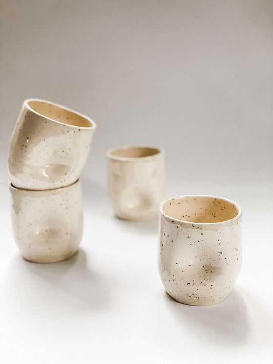 Four wheel thrown tumbler in cream clay with speckles with two dimples pinched into the sides