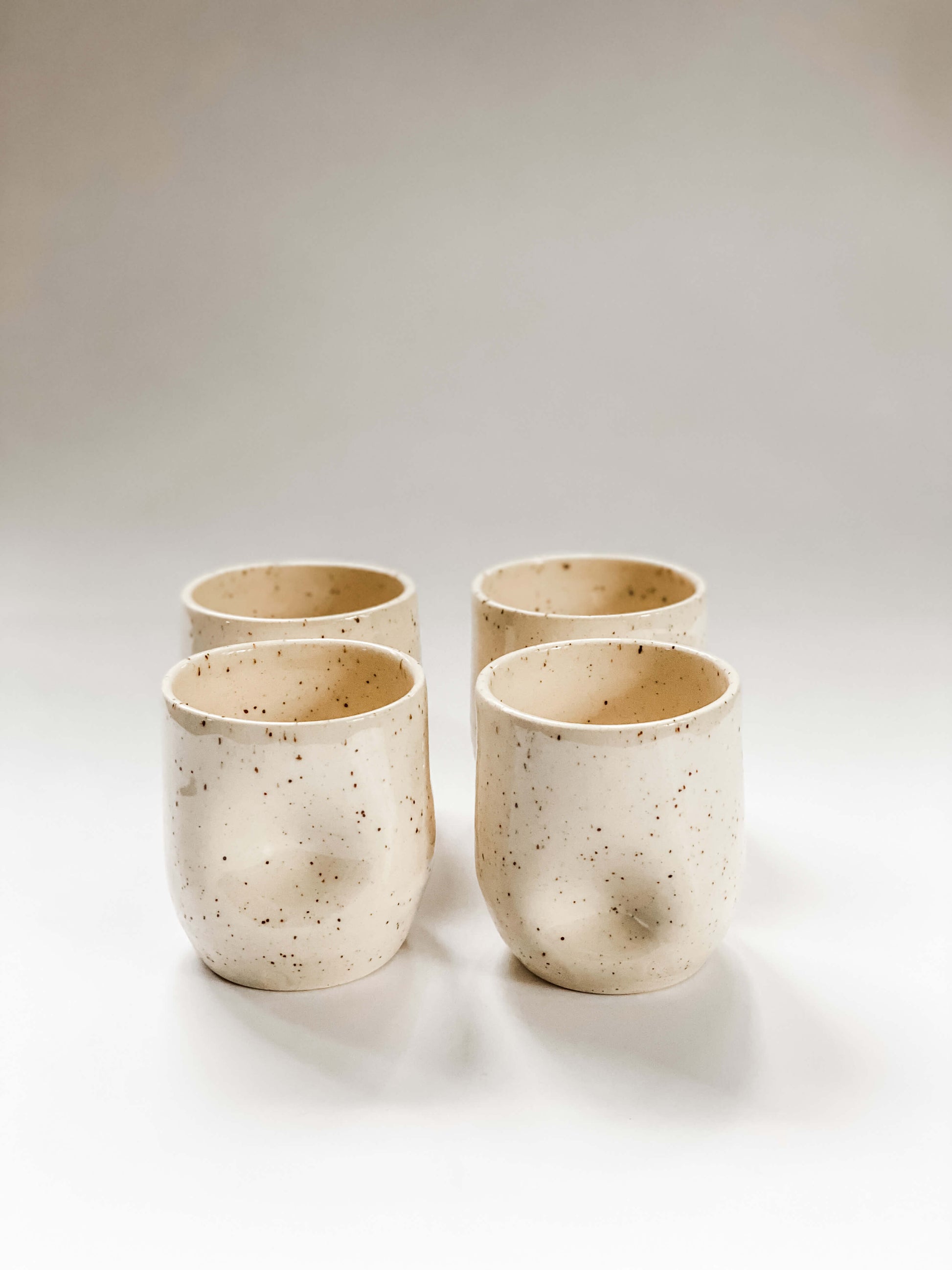 Four wheel thrown tumbler in cream clay with speckles with two dimples pinched into the sides