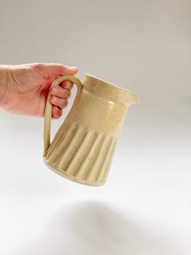 Wheel thrown, hand carved yellow speckled pitcher being held in a hand