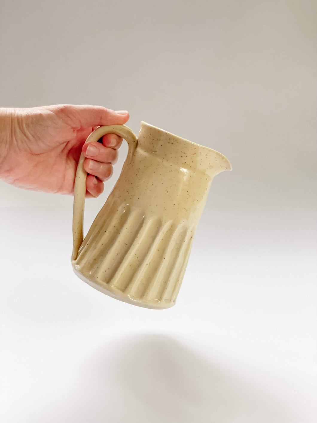 Wheel thrown, hand carved yellow speckled pitcher being held in a hand