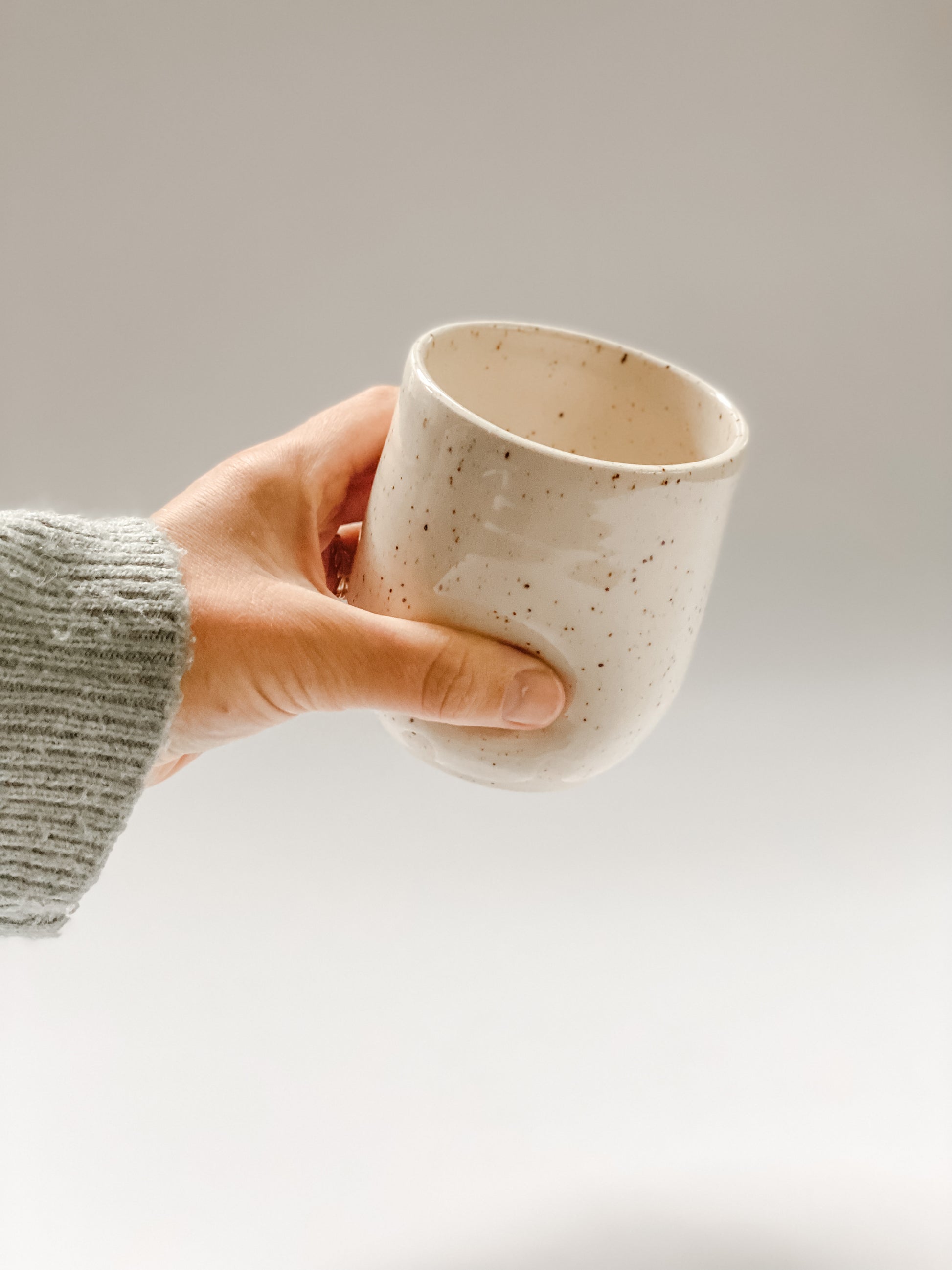 Hand picks up wheel thrown tumbler in cream clay with speckles with two dimples 