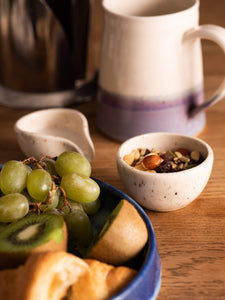 Blue ceramic plate with fruit, small cream and speckled wee bowl with nuts, purple and cream handmade mug in the background